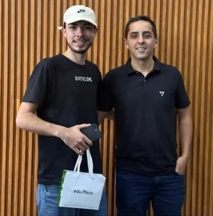 Dois clientes sorrindo na loja, um deles com o iPhone novo e a sacola da Edu.Place